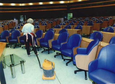 Schoonmaakster in vergaderzaal Tweede Kamer aan het stofzuigen